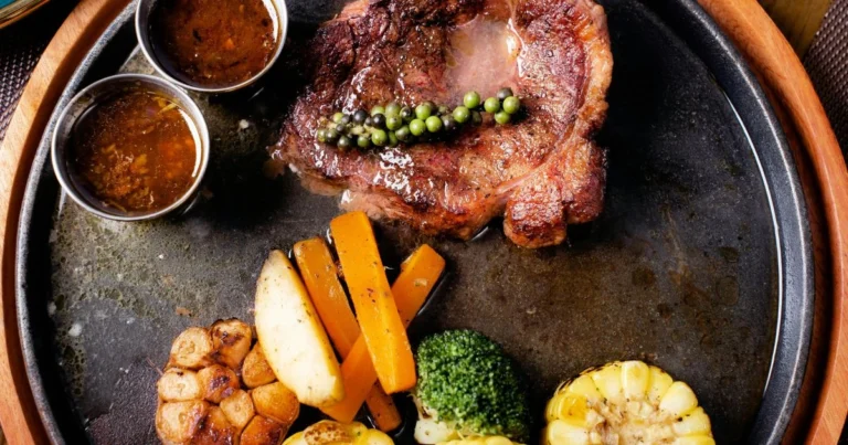 Indulge in a perfectly grilled steak served on a sizzling hot plate, accompanied by roasted vegetables, garlic, and flavorful sauces. A mouthwatering gourmet experience awaits!